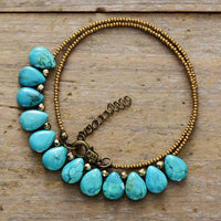 A Turquoise gemstone and seed bead necklace coiled on a wooden surface. ALLORA JADE