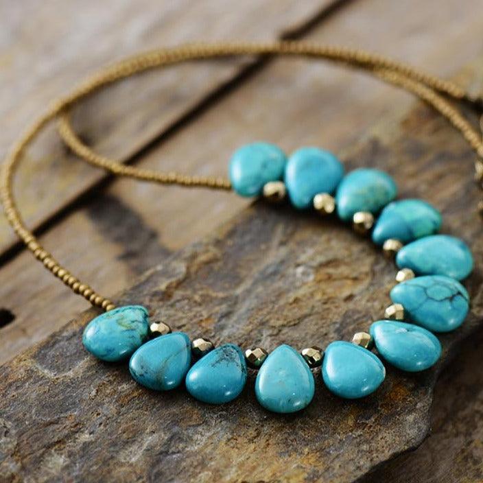 Close-up of A Turquoise gemstone and seed bead necklace laid out on a wooden surface. ALLORA JADE
