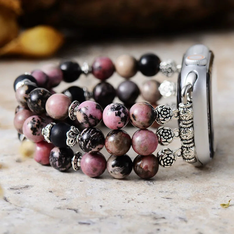 Stack of beaded bracelets with silver charms on a marble surface. Black Rhodonite Stretchy Apple Watch Band | ALLORA JADE
