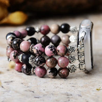 Stack of beaded bracelets with silver charms on a marble surface. Black Rhodonite Stretchy Apple Watch Band | ALLORA JADE