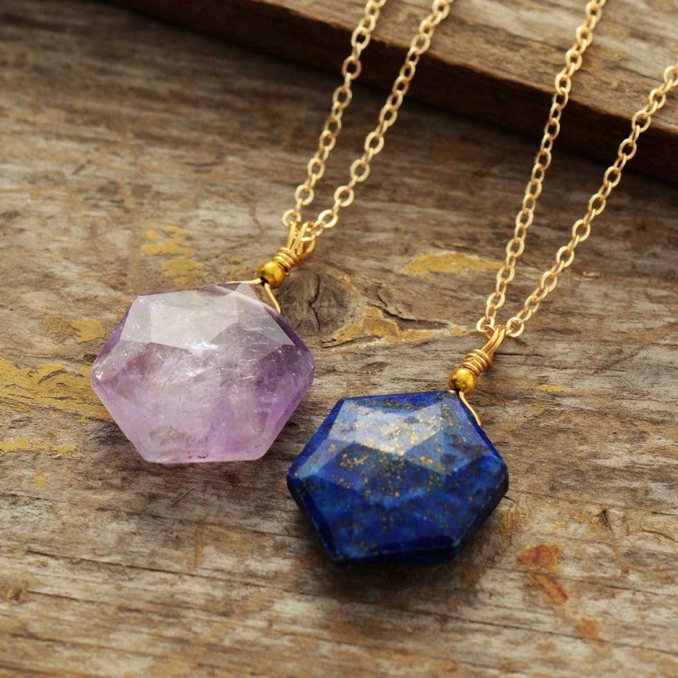 Close-up of Lapis Lazuli gemstone pendent with natural gold flecks and Amethyst pendant both on gold chain displayed on wooden surface- Allora Jade