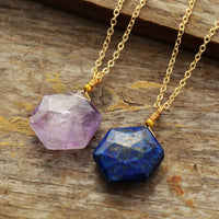Close-up of Lapis Lazuli gemstone pendent with natural gold flecks and Amethyst pendant both on gold chain displayed on wooden surface- Allora Jade