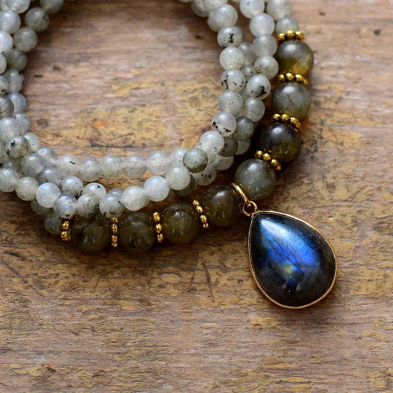 Labradorite Serenity Wrap Bracelet–Necklace coiled in a circle with iridescent teardrop pendant on rustic wood background. ALLORA JADE