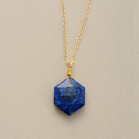 Close-up of Lapis Lazuli gemstone pendant with natural gold flecks on gold chain on grey background - Allora Jade