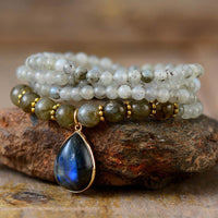 Handcrafted Labradorite Serenity Wrap Bracelet–Necklace coiled in a circle with iridescent teardrop pendant and mixed bead sizes on natural background. ALLOTA JADE