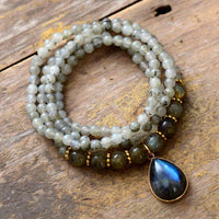 Handcrafted Labradorite Serenity Wrap Bracelet–Necklace coiled in a circle with iridescent teardrop pendant and mixed bead sizes on rustic wood background. ALLORA JADE