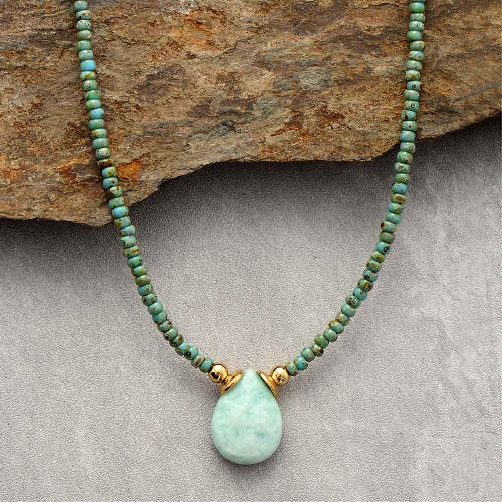 A green Amazonite teardrop-shaped pendant necklace with seed bead details, displayed on a rock. ALLORA JADE