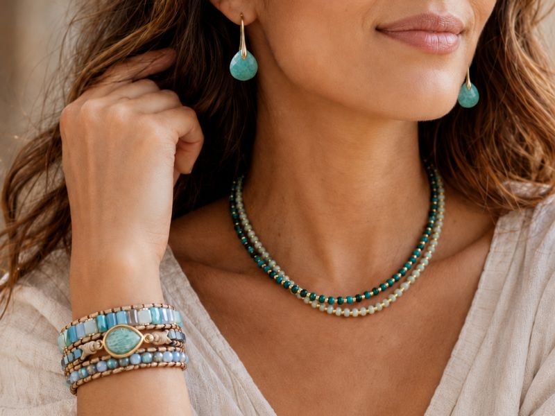 A close-up lifestyle shot of a woman wearing a multi-strand turquoise and white beaded necklace, matching teardrop earrings, and stacked bracelets on her wrist.