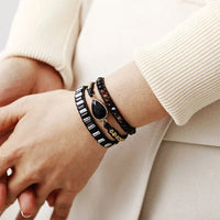 Close-up of a wrist wearing multiple bracelets black beaded bracelets with black Onyx charm. 