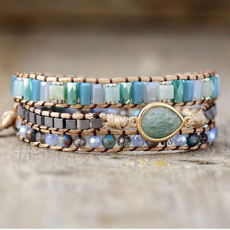 Multistrand beaded bracelet with a central Amazonite teardrop gemstone charm on a wooden surface