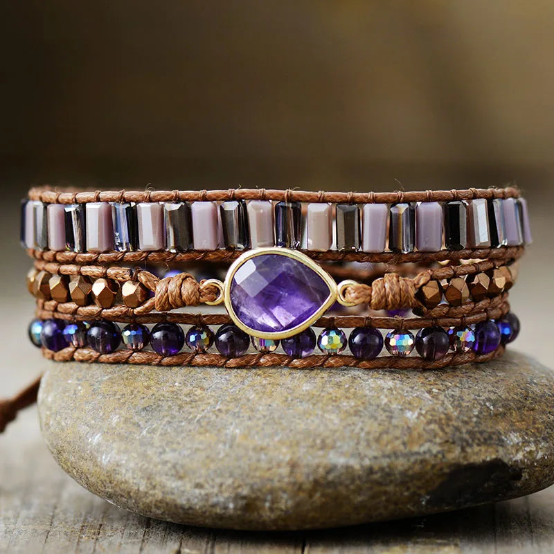 Multistrand beaded bracelet with an Amethyst gemstone charm, displayed on a stone surface