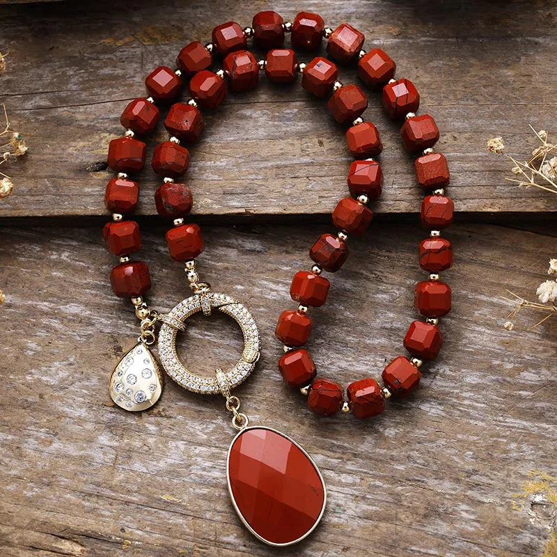 Red beaded necklace with a large red pendant on a wooden surface. Red Jasper Pavé Statement Necklace | ALLORA JADE