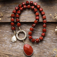 Red beaded necklace with a large red pendant on a wooden surface. Red Jasper Pavé Statement Necklace | ALLORA JADE