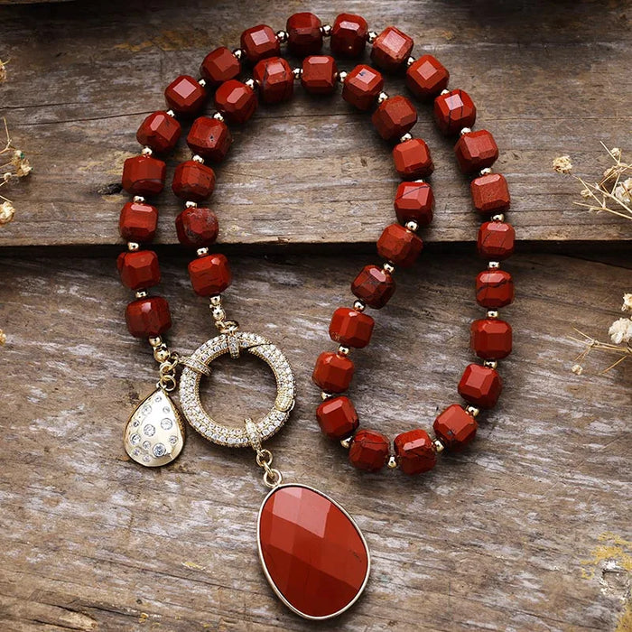Red beaded necklace with a large red pendant on a wooden surface. Red Jasper Pavé Statement Necklace | ALLORA JADE