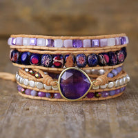 Multistrand beaded bracelet with Amethyst teardrop charm and purple beads on a wooden surface