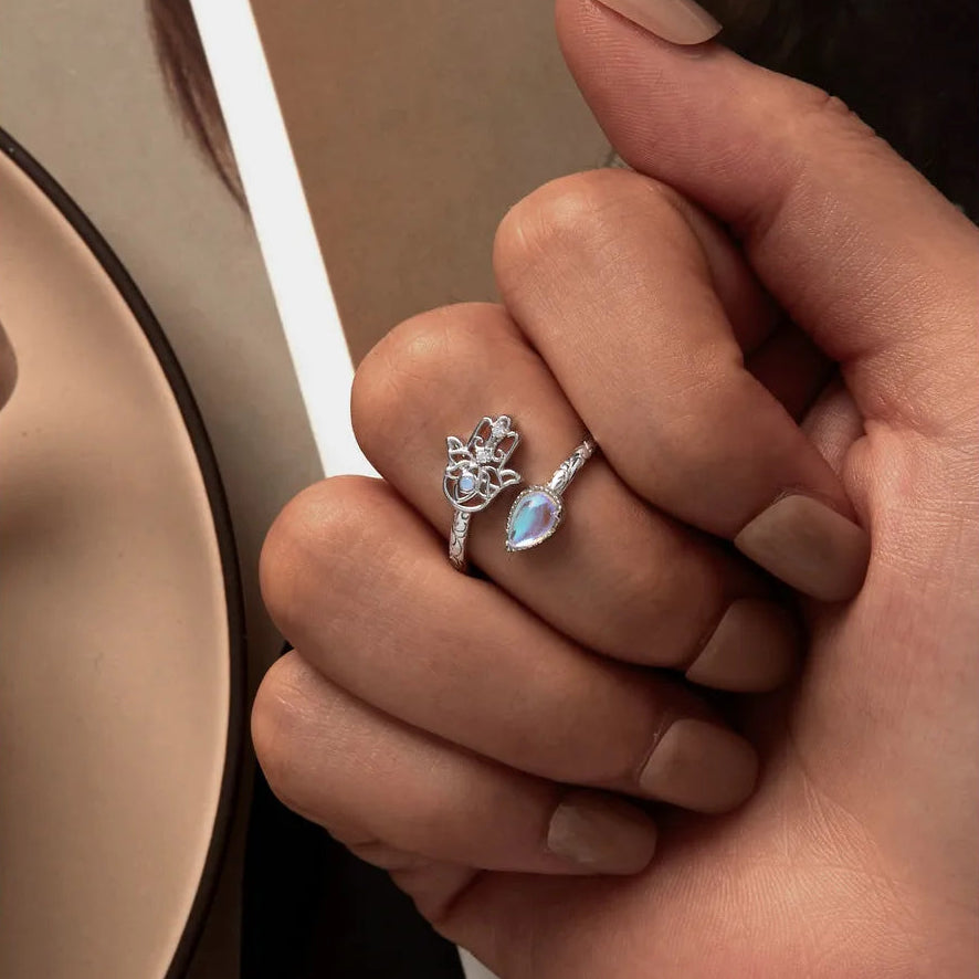 Close-up of a hand wearing a silver ring with a teardrop-shaped gemstone and Hamsa hand design, set against a neutral background.