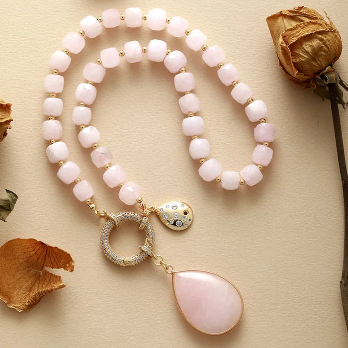 Necklace with pink beads and a teardrop pendant on a beige surface with dried flowers. Rose Quartz Pavé Statement Necklace | ALLORA JADE