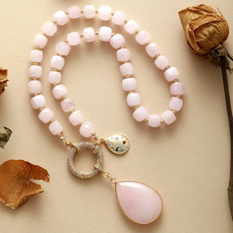 Necklace with pink beads and a teardrop pendant on a beige surface with dried flowers. Rose Quartz Pavé Statement Necklace | ALLORA JADE