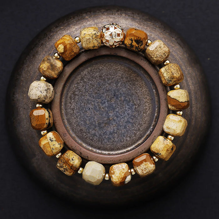 Bracelet with gold and brown beads on a dark background. Picture Jasper Faceted Cube Bracelet | ALLORA JADE