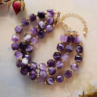 Purple beaded bracelet with gold accents on a textured surface