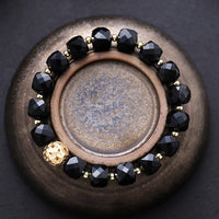 Bracelet with black beads and gold accents on a textured surface. Black Onyx Faceted Cube Bracelet | ALLORA JADE