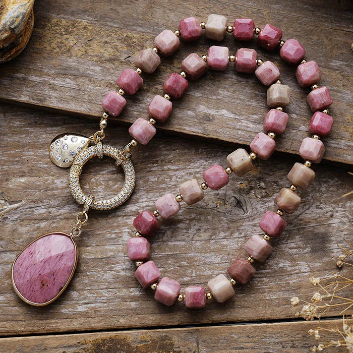 Necklace with pink beads and a large pink stone pendant on a wooden surface. Rhodonite Pavé Statement Necklace | ALLORA JADE