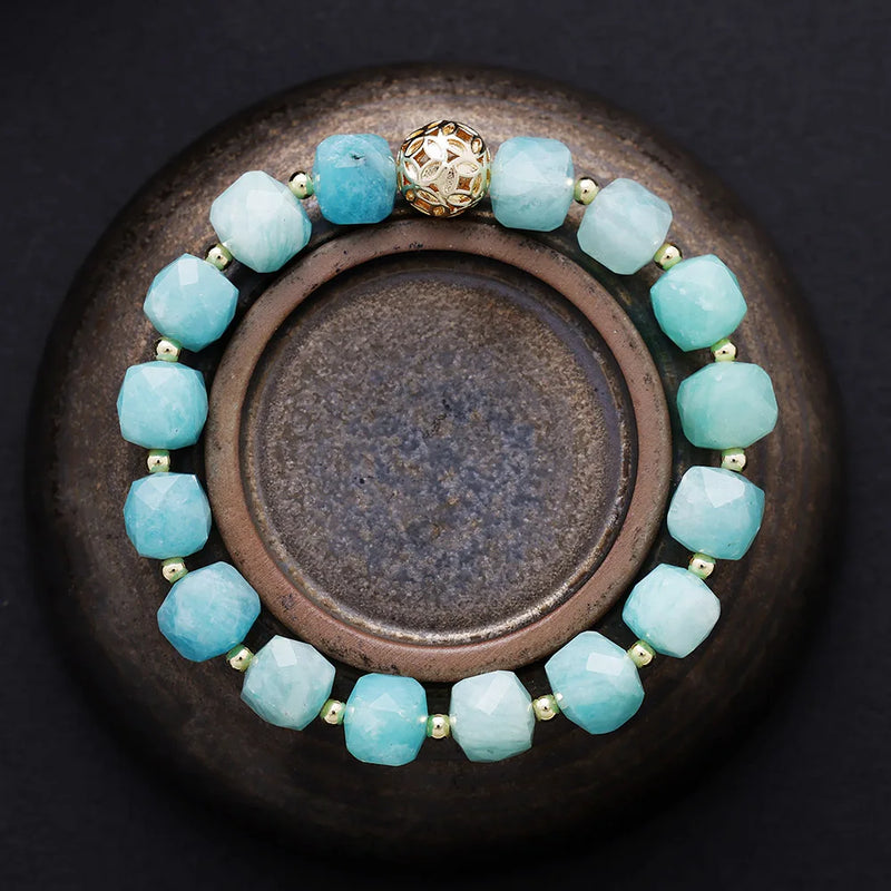 Aqua beaded bracelet with a gold clasp on a dark surface. Amazonite Faceted Cube Bracelet - ALLORA JADE