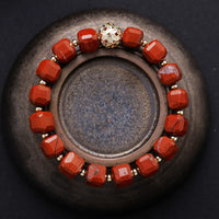 Bracelet with red beads and a gold accent on a dark surface. Red Jasper Faceted Cube Bracelet | ALLORA JADE