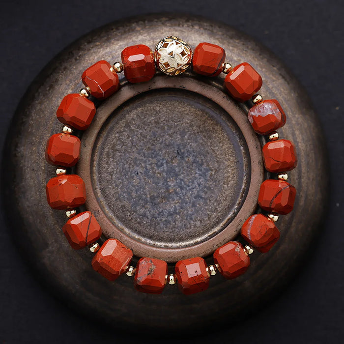 Bracelet with red beads and a gold accent on a dark surface. Red Jasper Faceted Cube Bracelet | ALLORA JADE