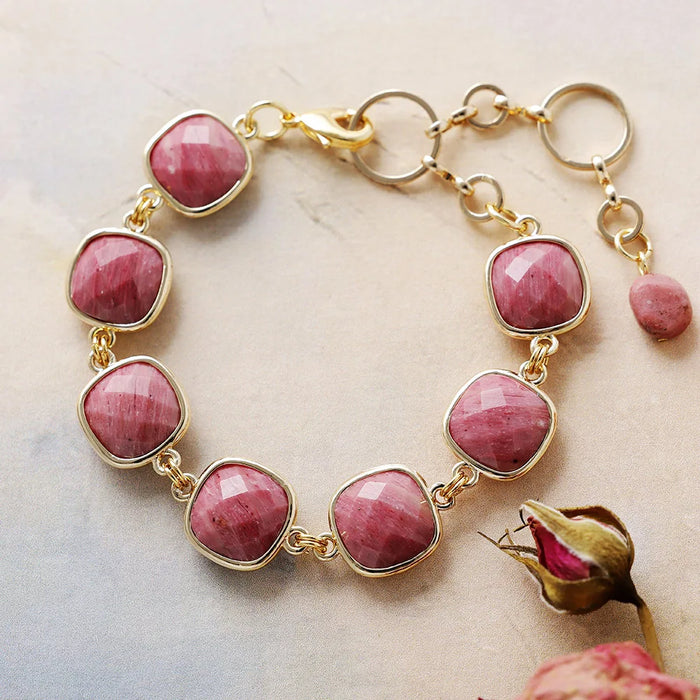Gold bracelet with pink gemstones on a marble surface with a dried rose.