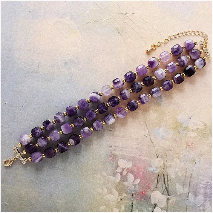 3-strand Purple Amethyst beaded bracelet with gold accents displayed flat on a textured surface.