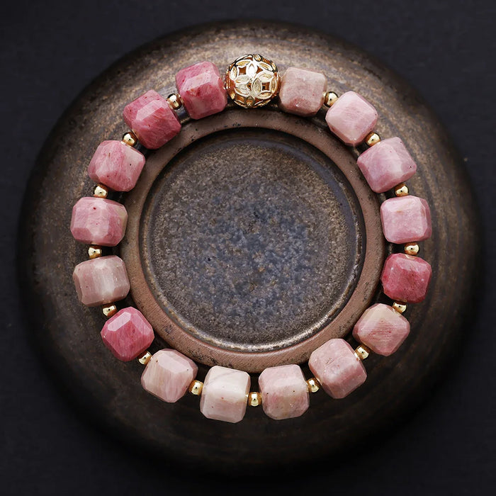 Bracelet with pink beads and a gold clasp on a dark background. Rhodonite Faceted Cube Bracelet | ALLORA JADE