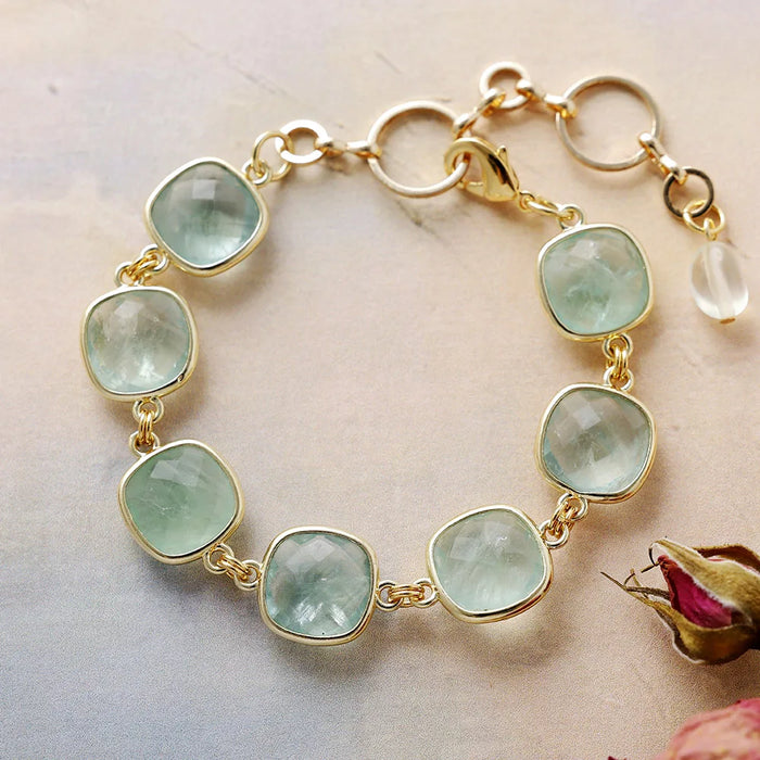 Gold bracelet with green gemstones on a light background