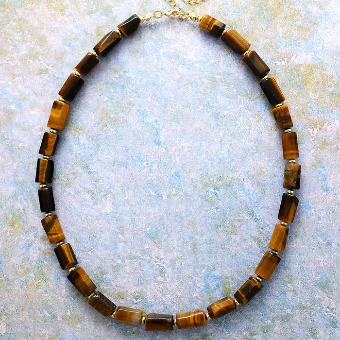 Necklace with brown and gold beads on a textured light blue background. ALLORA JADE