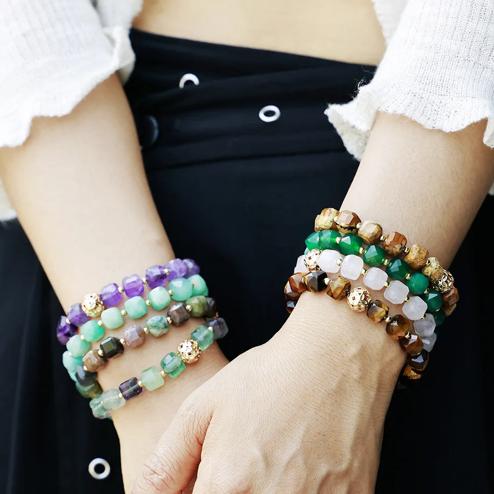 Close-up of hands wearing multiple beaded bracelets on a plain background. Faceted Cube Bracelet | ALLORA JADE