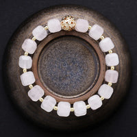 Bracelet with soft pink beads and a gold clasp on a dark surface. Rose Quartz Faceted Cube Bracelet | ALLORA JADE