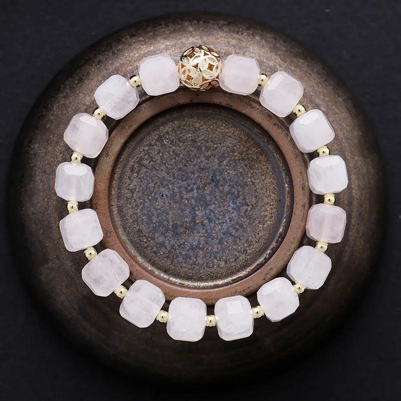 Bracelet with soft pink beads and a gold clasp on a dark surface. Rose Quartz Faceted Cube Bracelet | ALLORA JADE