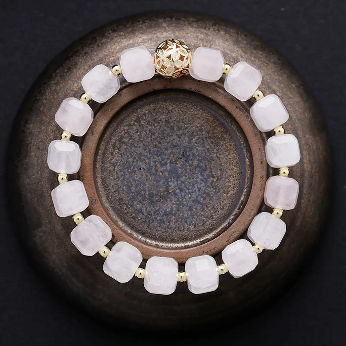 Bracelet with soft pink beads and a gold clasp on a dark surface. Rose Quartz Faceted Cube Bracelet | ALLORA JADE
