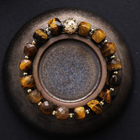Bracelet with brown beads on a dark surface. Tiger’s Eye Faceted Cube Bracelet | ALLORA JADE