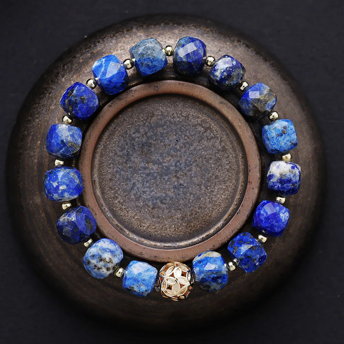 Bracelet with blue beads and a gold accent on a dark surface. Lapis Lazuli Faceted Cube Bracelet | ALLORA JADE