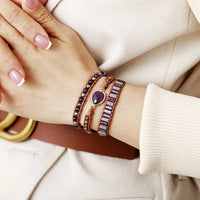 Close-up of a wrist wearing multiple bracelets with an Amethyst charm, shown on a neutral background