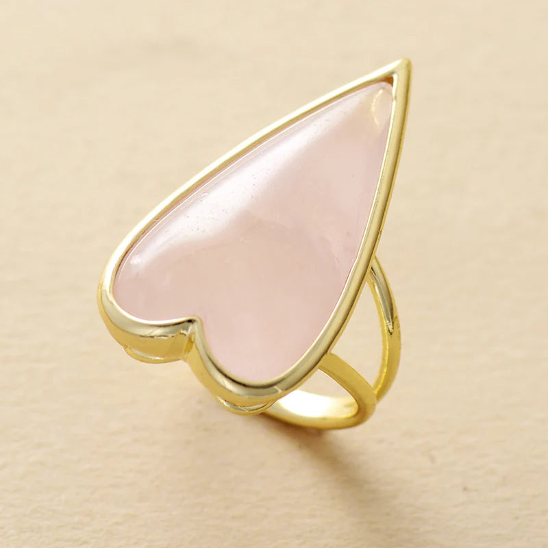 Gold ring with a heart-shaped pink Rose Quartz gemstone on a beige background