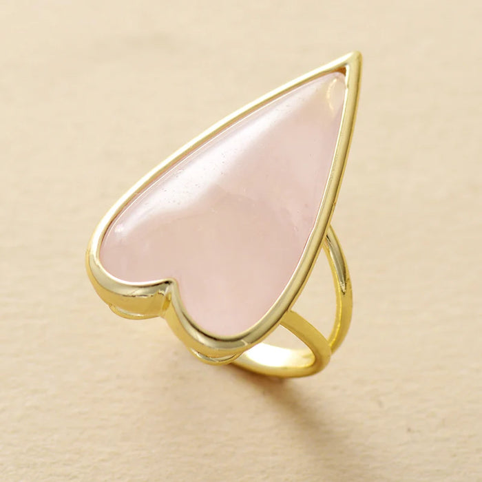 Gold ring with a heart-shaped pink Rose Quartz gemstone on a beige background