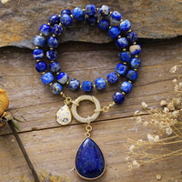 Blue beaded necklace with gold accents and pendant on a wooden surface. Lapis Lazuli Pavé Statement Necklace | ALLORA JADE