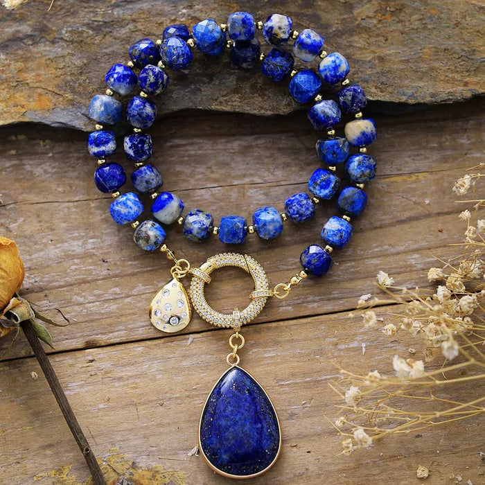 Blue beaded necklace with gold accents and pendant on a wooden surface. Lapis Lazuli Pavé Statement Necklace | ALLORA JADE