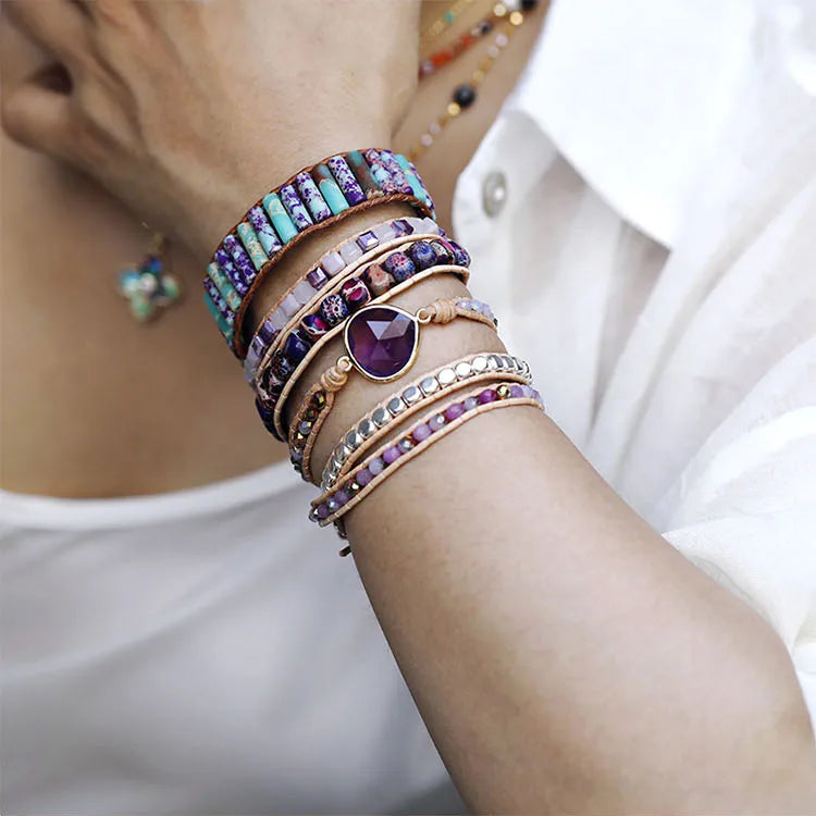 Close-up of a hand wearing multiple bracelets with purple stones on a blurred background