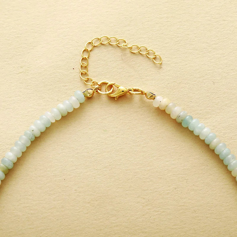 Necklace with light green beads and gold clasp on a beige background