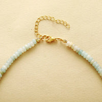 Necklace with light green beads and gold clasp on a beige background