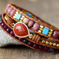 Multicolored beaded bracelet with Red Jasper charm, displayed on a textured surface
