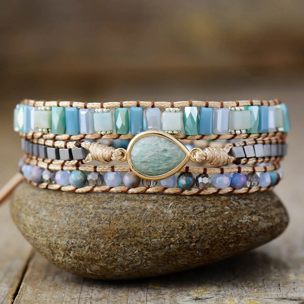 Multistrand beaded bracelet with a central Amazonite teardrop gemstone charm on a stone surface